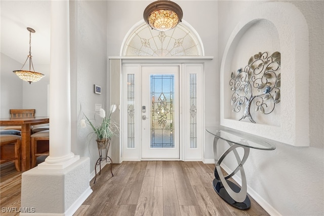 foyer with a towering ceiling, wood-type flooring, and ornate columns