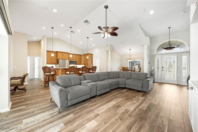 living room featuring ornate columns, ceiling fan, high vaulted ceiling, and light wood-type flooring