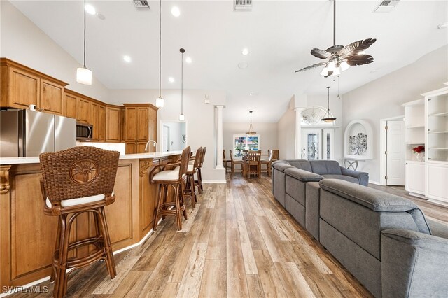 kitchen with appliances with stainless steel finishes, light hardwood / wood-style flooring, a kitchen breakfast bar, and decorative light fixtures