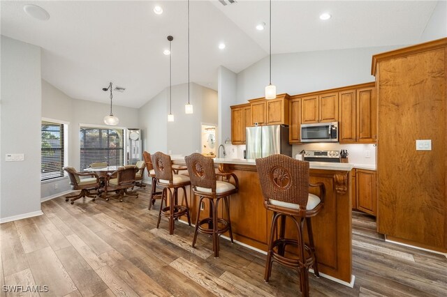 kitchen with dark wood-type flooring, a kitchen bar, high vaulted ceiling, pendant lighting, and stainless steel appliances