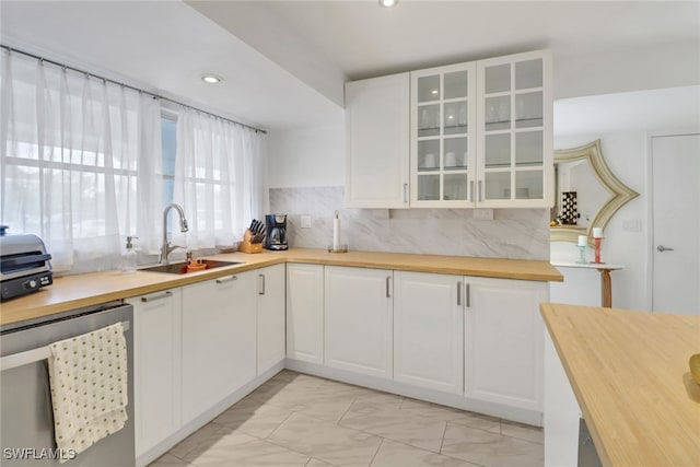 kitchen with tasteful backsplash, white cabinetry, sink, butcher block counters, and stainless steel dishwasher