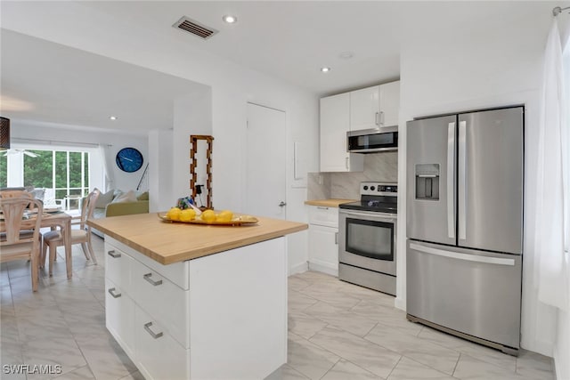 kitchen featuring white cabinetry, wooden counters, a center island, appliances with stainless steel finishes, and decorative backsplash