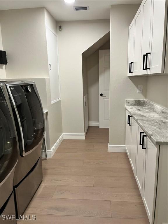 laundry room with cabinets, washer and clothes dryer, and light wood-type flooring