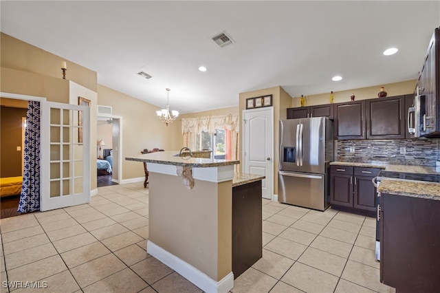 kitchen with a breakfast bar, stainless steel fridge with ice dispenser, hanging light fixtures, a kitchen island with sink, and backsplash