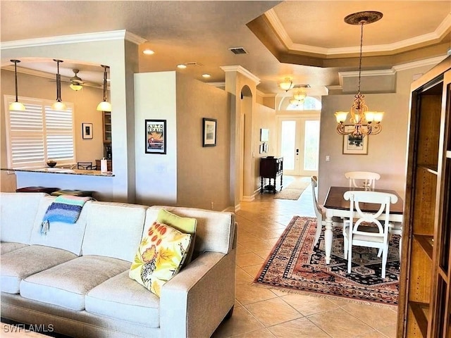 tiled living room with a tray ceiling, crown molding, french doors, and a chandelier