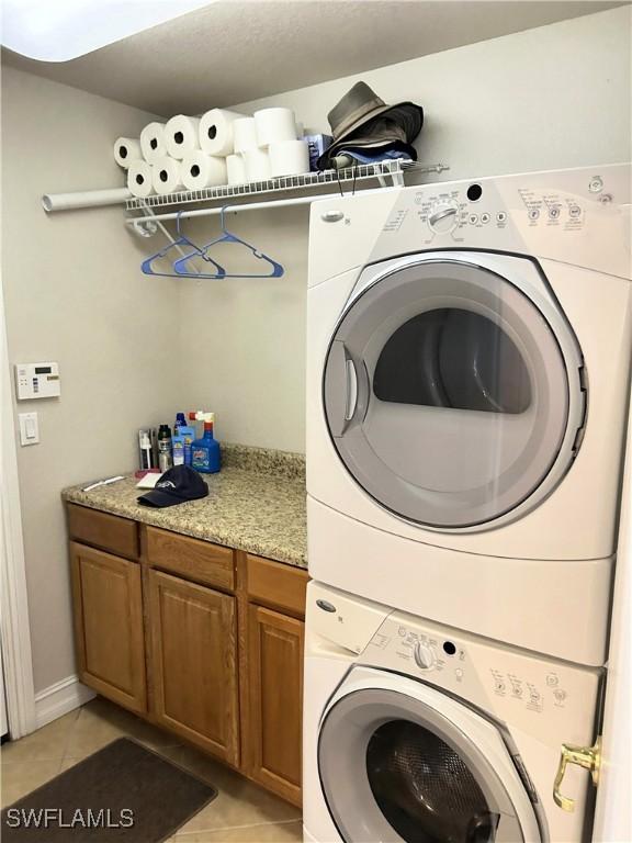 clothes washing area with light tile patterned flooring, cabinets, and stacked washer and clothes dryer