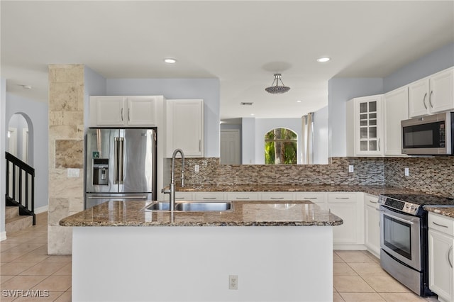 kitchen with stainless steel appliances, sink, a center island with sink, and dark stone countertops