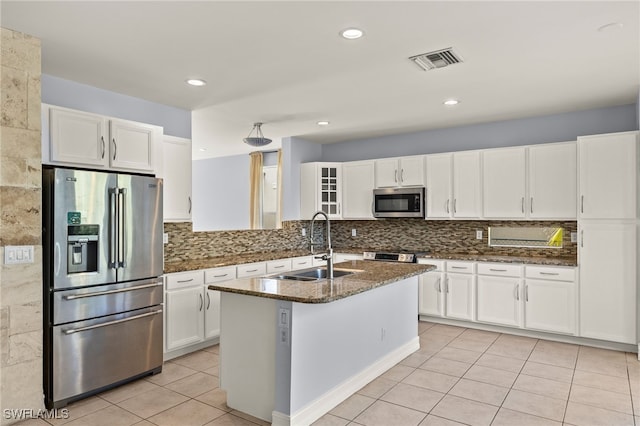 kitchen featuring appliances with stainless steel finishes, white cabinetry, sink, dark stone countertops, and a kitchen island with sink