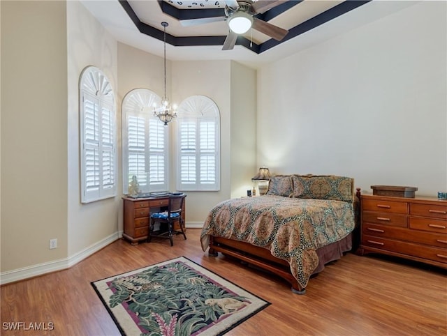 bedroom featuring a tray ceiling, hardwood / wood-style floors, and ceiling fan with notable chandelier