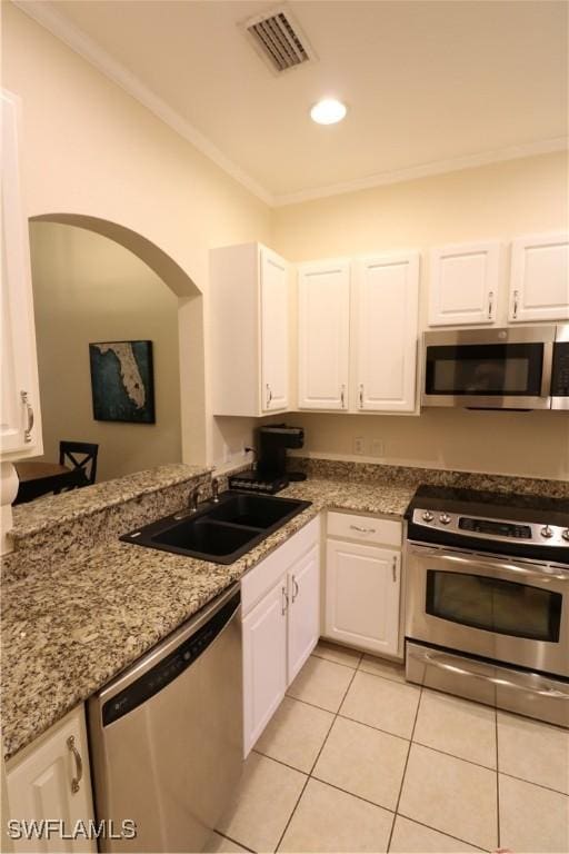 kitchen with appliances with stainless steel finishes, white cabinetry, sink, light tile patterned floors, and light stone counters