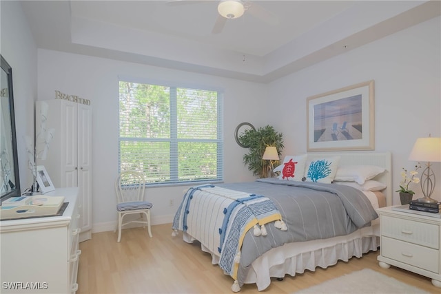 bedroom with a raised ceiling, ceiling fan, and light hardwood / wood-style flooring