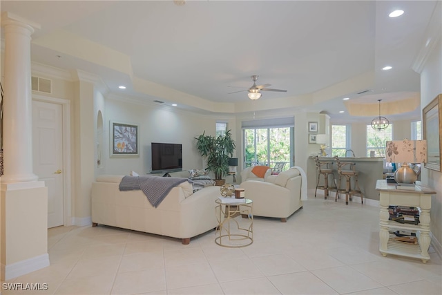 tiled living room featuring crown molding, a tray ceiling, ceiling fan, and ornate columns