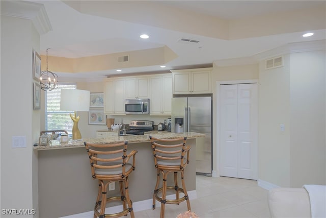 kitchen with hanging light fixtures, stainless steel appliances, a kitchen breakfast bar, light stone counters, and cream cabinets