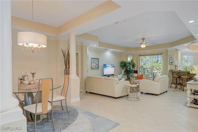 living area featuring ceiling fan with notable chandelier, a tray ceiling, recessed lighting, light tile patterned floors, and decorative columns