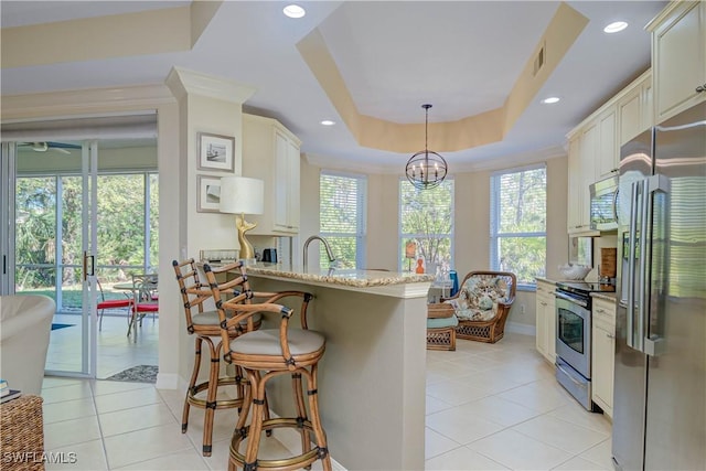 kitchen with light stone counters, appliances with stainless steel finishes, a peninsula, light tile patterned flooring, and a raised ceiling