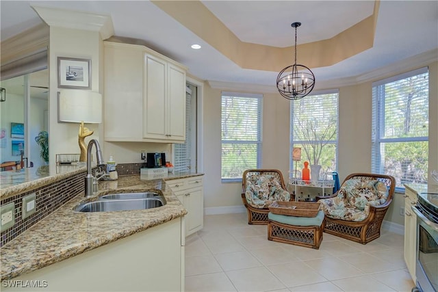 kitchen featuring a sink, a tray ceiling, decorative light fixtures, light stone countertops, and a chandelier