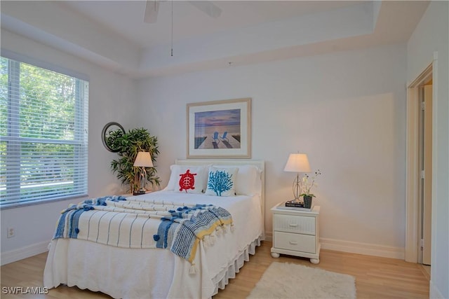 bedroom with a ceiling fan, a raised ceiling, light wood-style floors, and baseboards