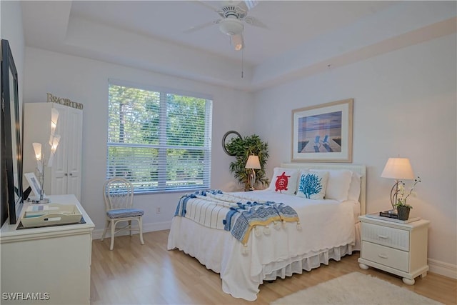 bedroom with baseboards, a raised ceiling, light wood-style floors, and ceiling fan