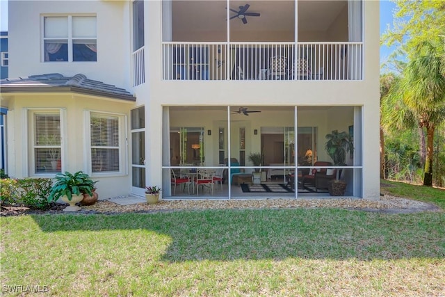 back of property with stucco siding, a lawn, a ceiling fan, and a sunroom