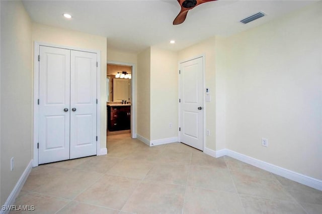 unfurnished bedroom featuring a closet, light tile patterned floors, ceiling fan, and ensuite bath