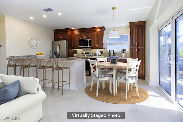 kitchen featuring a breakfast bar area, hanging light fixtures, stainless steel appliances, light stone countertops, and decorative backsplash