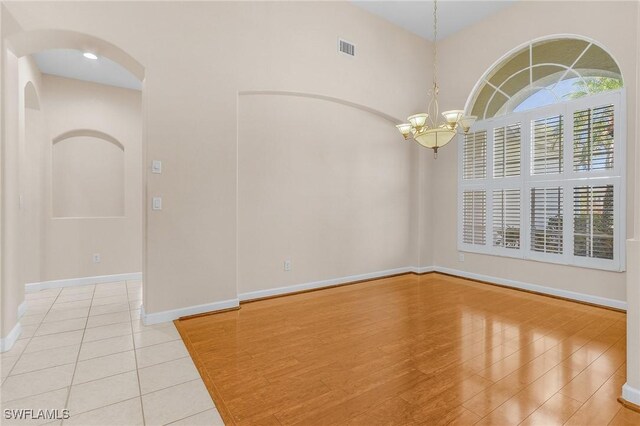 spare room featuring a chandelier, arched walkways, light tile patterned flooring, visible vents, and baseboards