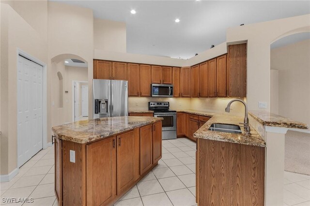 kitchen featuring sink, light tile patterned floors, appliances with stainless steel finishes, kitchen peninsula, and light stone countertops