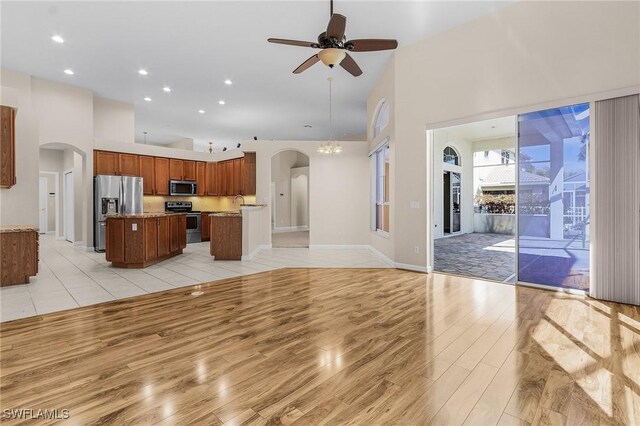 unfurnished living room featuring arched walkways, ceiling fan, a high ceiling, and light wood-type flooring