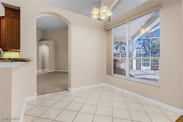 unfurnished dining area featuring arched walkways, light tile patterned floors, a notable chandelier, light carpet, and baseboards