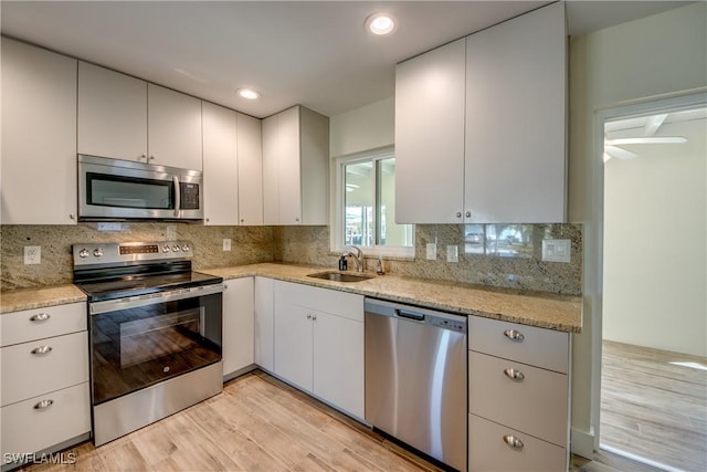 kitchen with tasteful backsplash, stainless steel appliances, light stone countertops, and sink