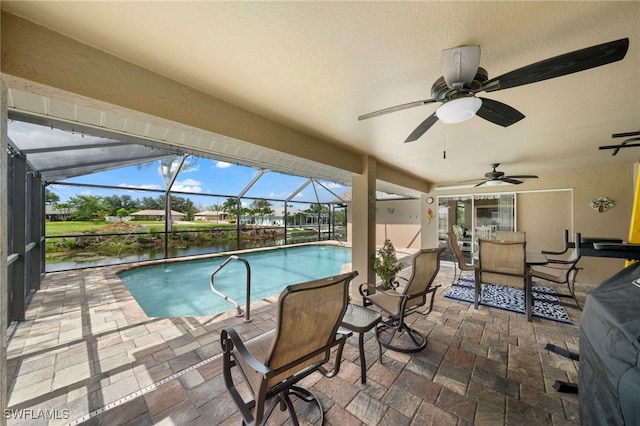 view of pool featuring ceiling fan, a patio, glass enclosure, and a water view