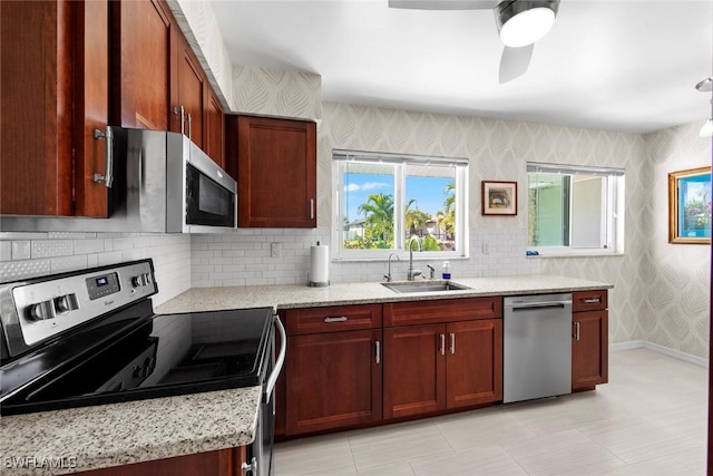 kitchen with sink, ceiling fan, appliances with stainless steel finishes, light stone counters, and decorative backsplash