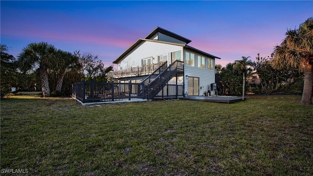 back house at dusk featuring a lawn and a deck