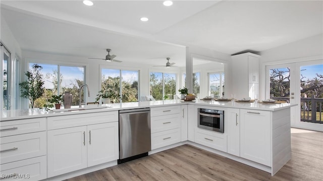 kitchen featuring appliances with stainless steel finishes, white cabinetry, sink, kitchen peninsula, and light hardwood / wood-style flooring