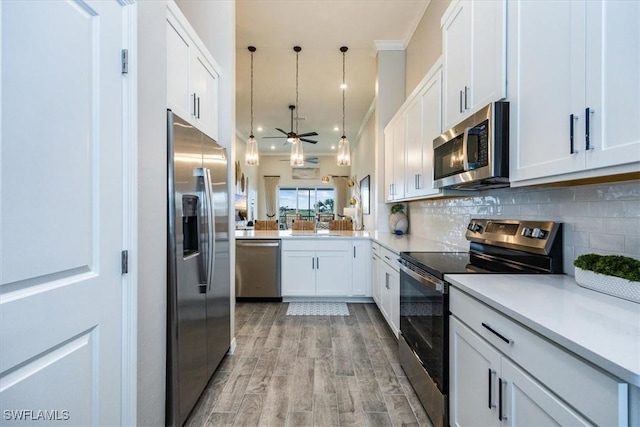 kitchen featuring appliances with stainless steel finishes, white cabinetry, decorative backsplash, decorative light fixtures, and kitchen peninsula