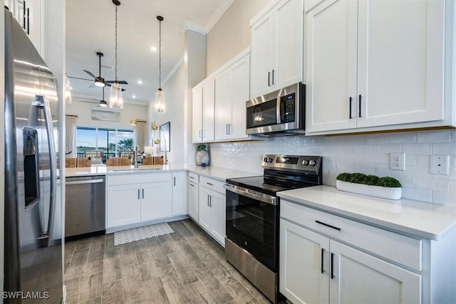 kitchen with pendant lighting, white cabinets, kitchen peninsula, stainless steel appliances, and crown molding