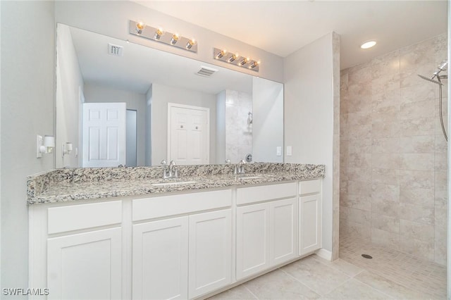 full bath featuring double vanity, visible vents, a tile shower, and a sink