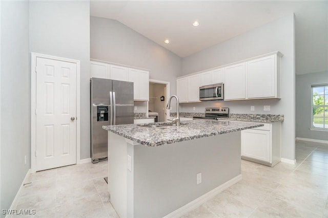 kitchen featuring stainless steel appliances, a sink, white cabinetry, light stone countertops, and an island with sink