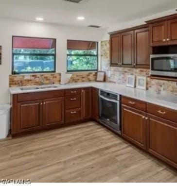 kitchen with stainless steel appliances, light hardwood / wood-style floors, sink, and backsplash