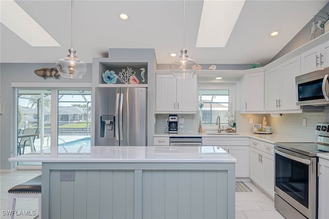 kitchen with lofted ceiling with skylight, sink, white cabinetry, appliances with stainless steel finishes, and pendant lighting