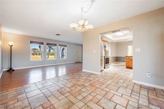 empty room featuring a raised ceiling, a textured ceiling, and a notable chandelier