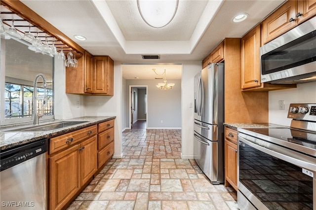 kitchen with sink, dark stone countertops, an inviting chandelier, stainless steel appliances, and a tray ceiling