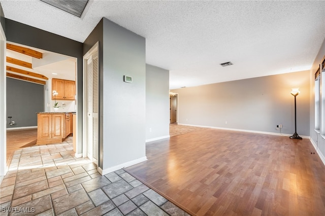 empty room featuring beamed ceiling, a textured ceiling, and light hardwood / wood-style flooring