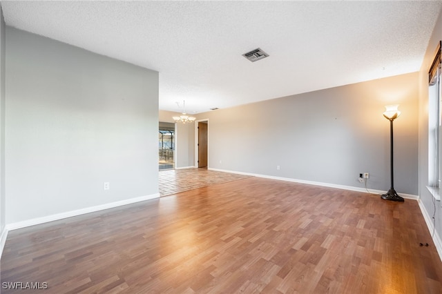 spare room with wood-type flooring, a textured ceiling, and a notable chandelier