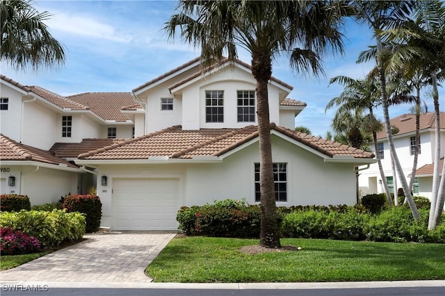 view of front of house with a garage, driveway, a tiled roof, a front lawn, and stucco siding