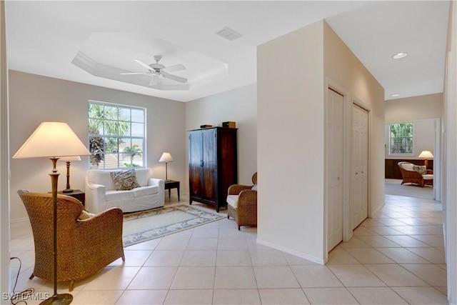 living area with light tile patterned floors, ceiling fan, a tray ceiling, and baseboards