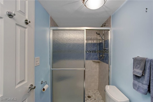 bathroom featuring a shower with door and toilet