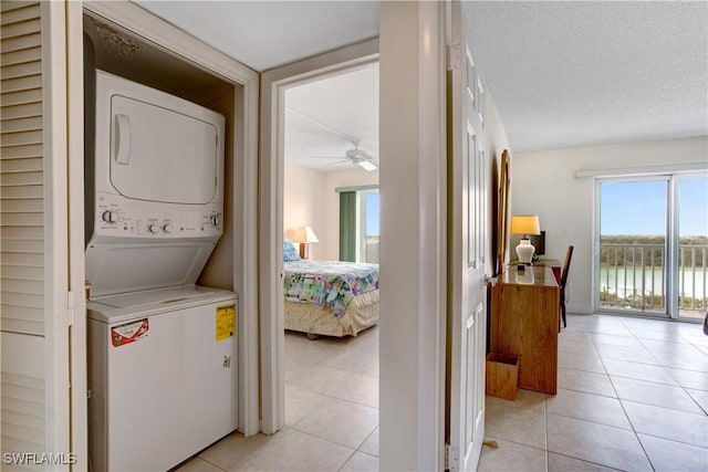 clothes washing area featuring ceiling fan, stacked washer and dryer, a textured ceiling, and light tile patterned floors