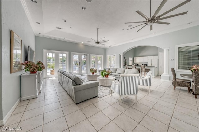 tiled living room featuring crown molding, ceiling fan, french doors, a raised ceiling, and ornate columns