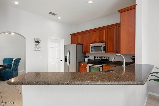 kitchen with light tile patterned flooring, appliances with stainless steel finishes, sink, dark stone countertops, and kitchen peninsula